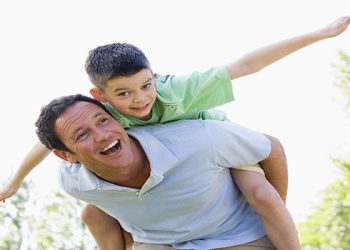 Woman giving son piggy back in park