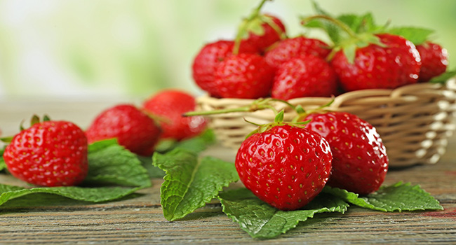 Ripe strawberries with leaves on wooden table, closeup