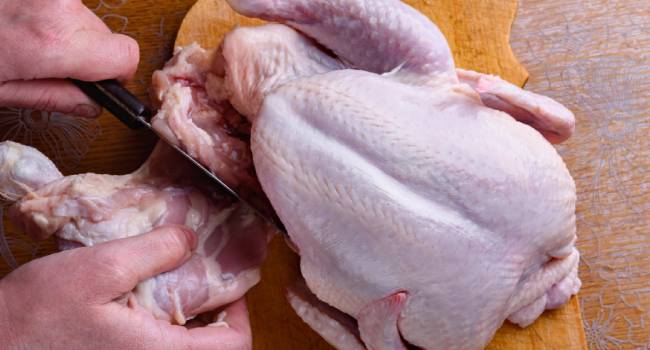 Female hands carves a whole chicken carcass on a wooden board. Top view.