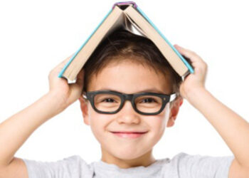 Cute little child plays with book while wearing glasses, isolated over white