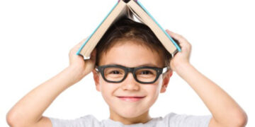 Cute little child plays with book while wearing glasses, isolated over white